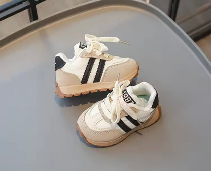 Pair of children's sneakers with black stripes on a gray surface