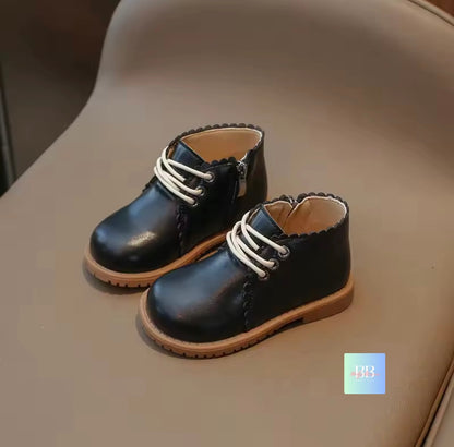 Pair of black children's shoes with white laces on a beige surface