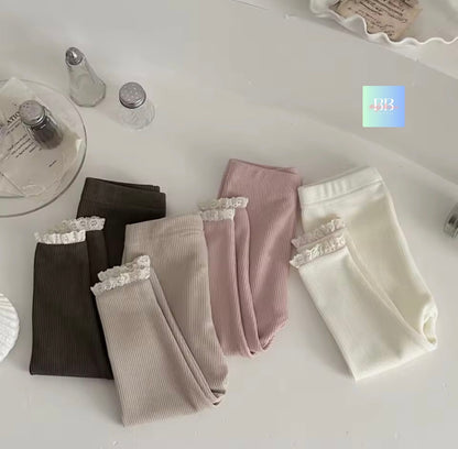 Four pairs of ribbed leggings with lace trim in black, gray, pink, and white on a white surface.