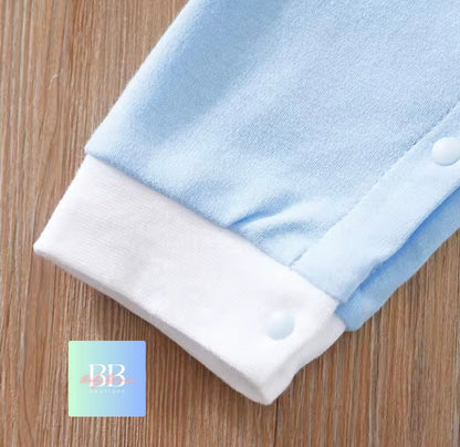 Folded baby onesie with blue top and white bottom on a wooden surface, featuring a brand logo in the corner.