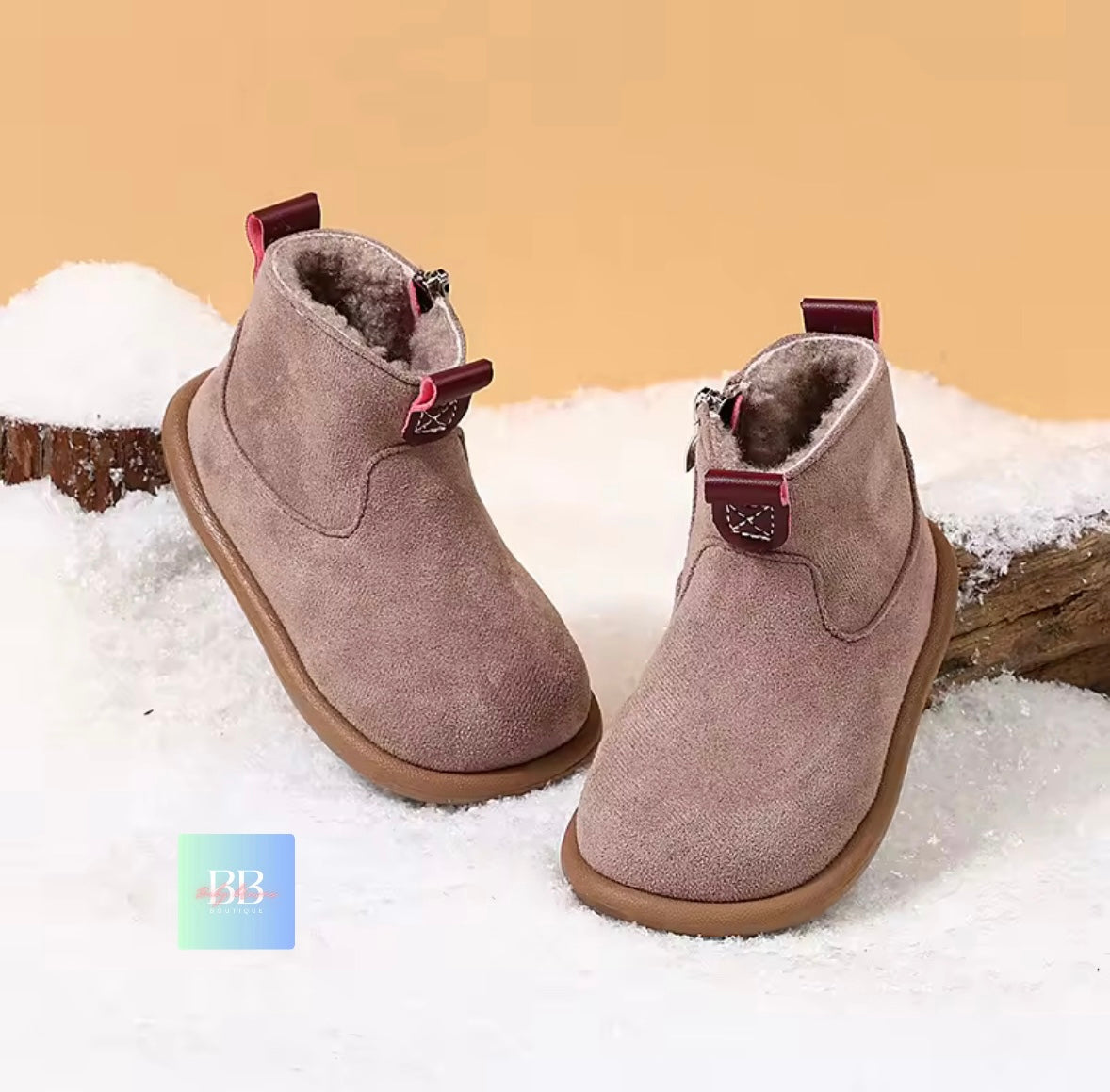 Pair of brown suede boots with red buckles on a snowy background