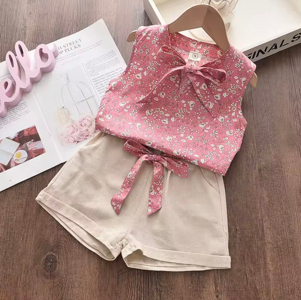 Pink floral top and beige shorts on a wooden surface with a magazine underneath.