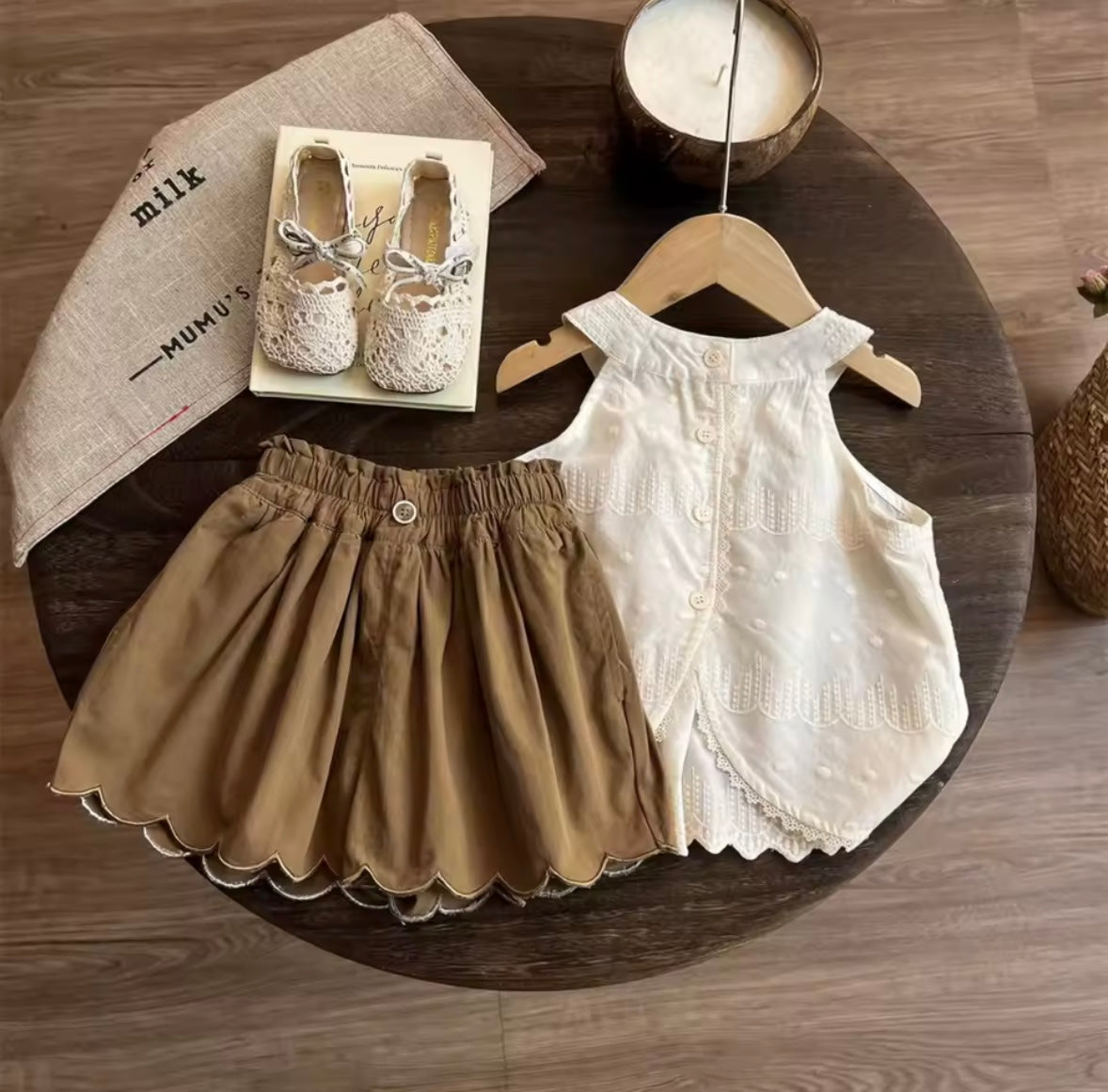 Children's clothing including a white top, brown shorts, and shoes on a wooden table.