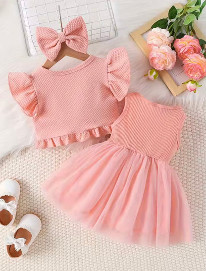 Pink children's dress with matching headband on a textured surface with flowers and shoes.