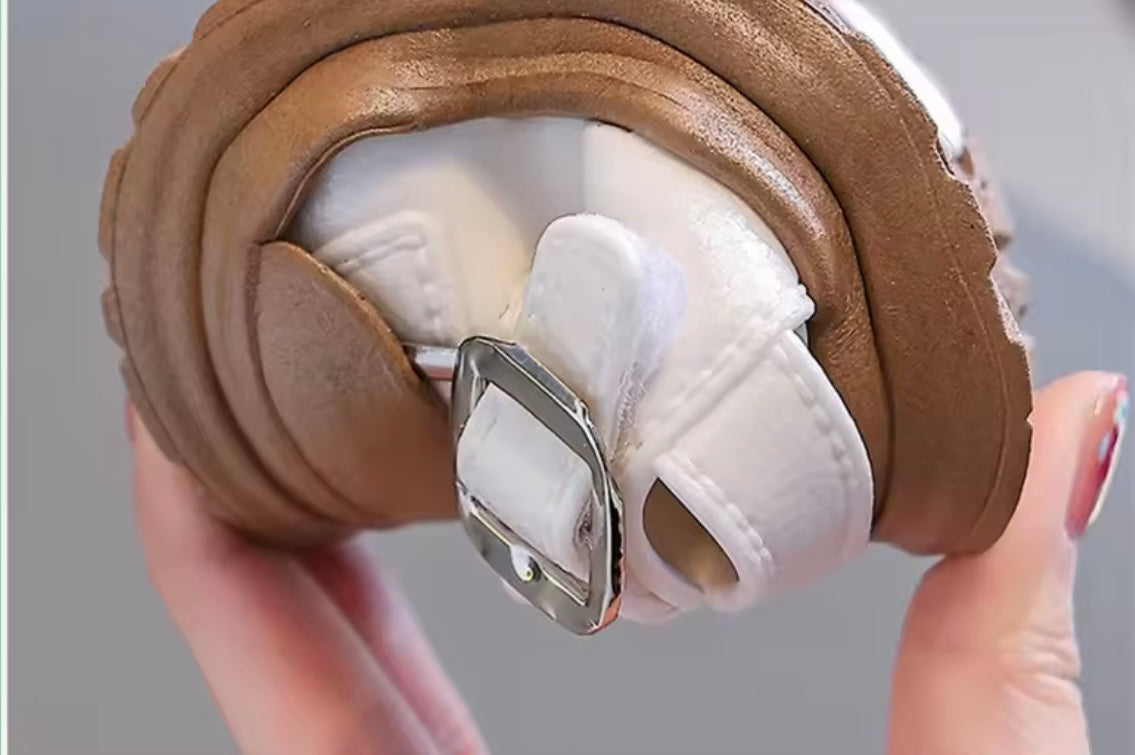 Close-up of a brown shoe with a white sole held by a hand against a gray background