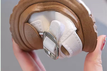 Close-up of a brown shoe with a white sole held by a hand against a gray background