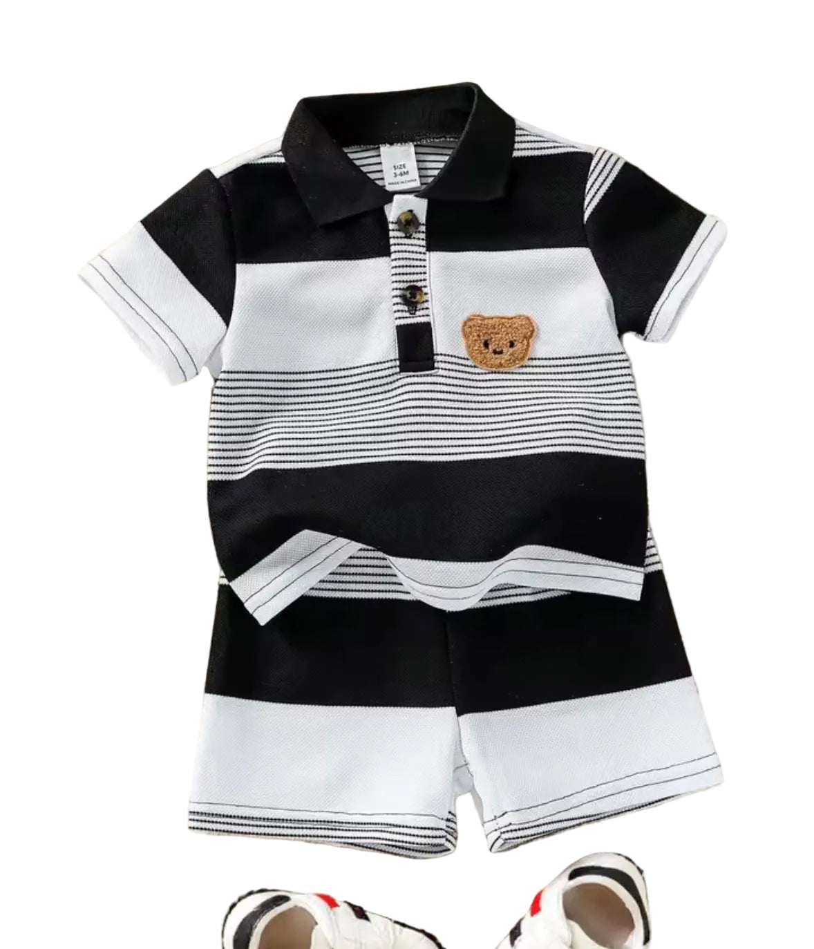 Children's black and white striped polo shirt with bear design and shorts on a textured surface.