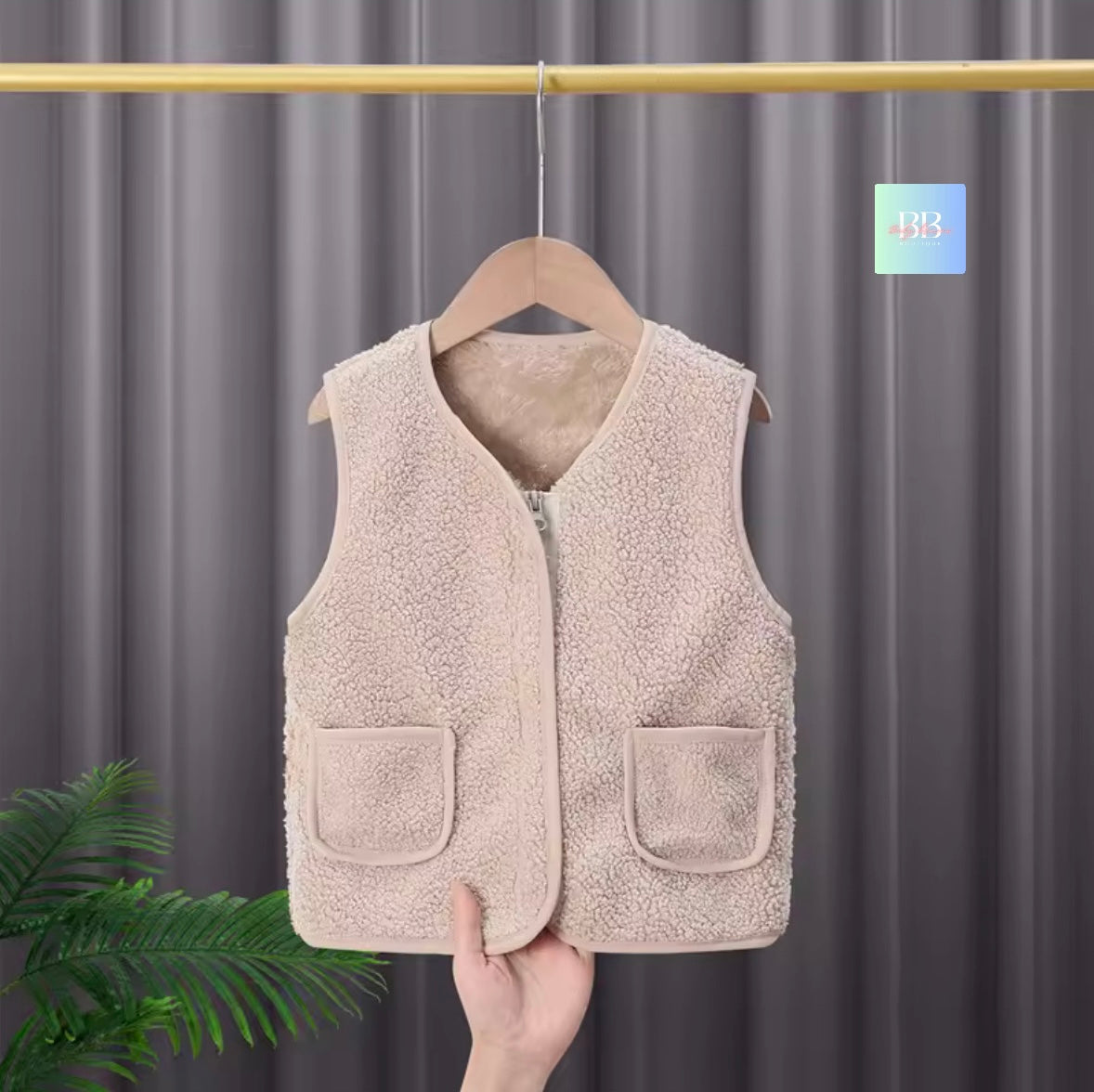 Beige fleece vest on a hanger against a gray curtain background