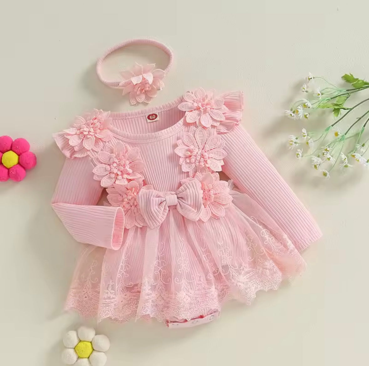 Pink baby dress with floral details and headband on a light background
