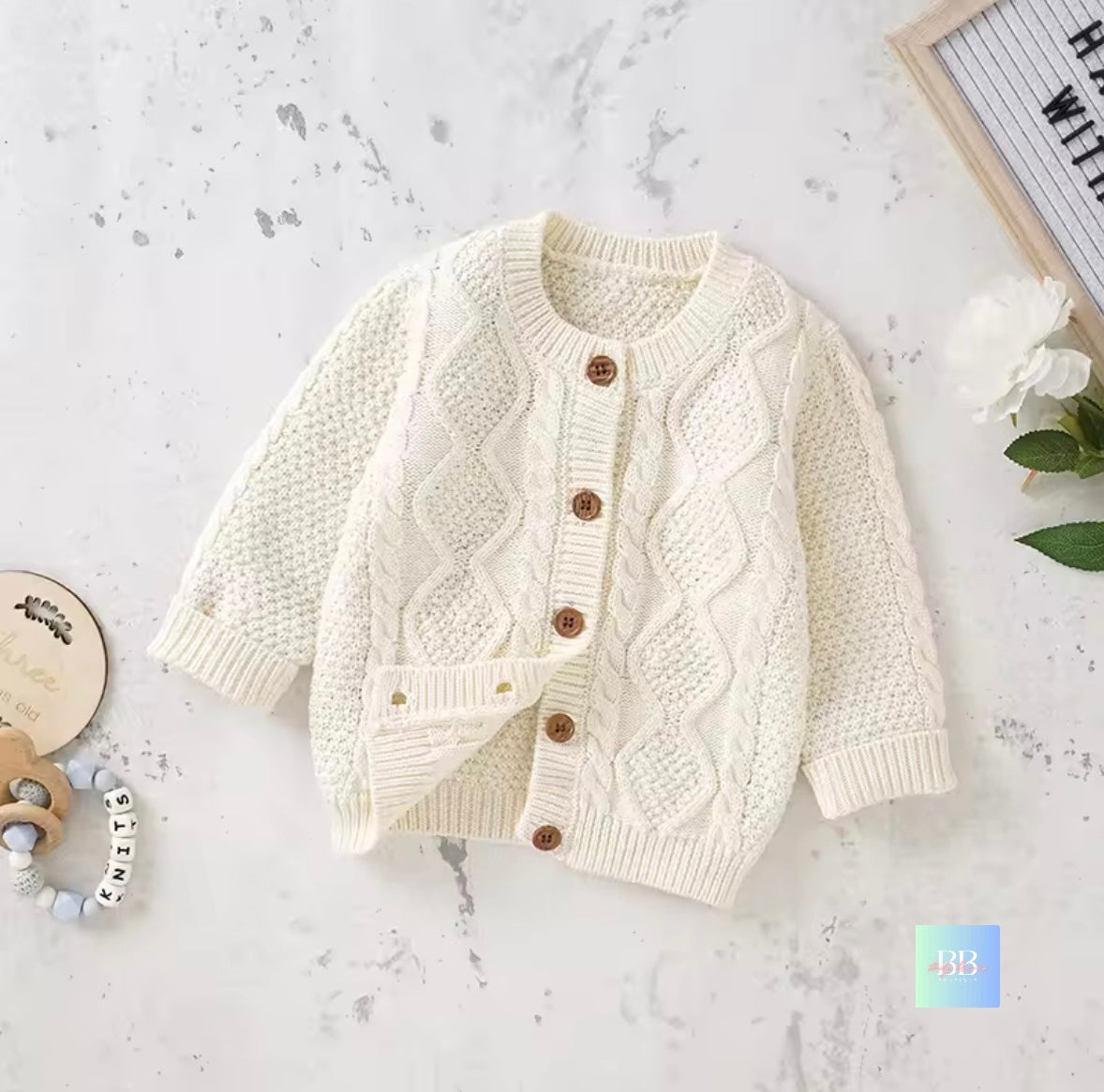 White knitted cardigan with brown buttons on a light gray surface.