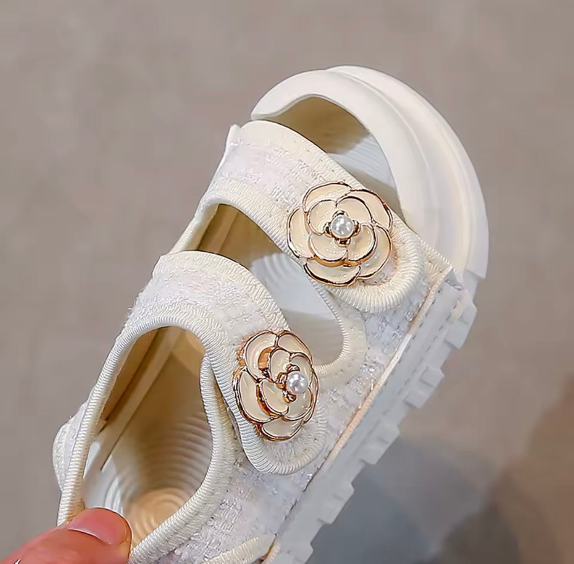 White sandal with floral embellishments held by a hand against a neutral background