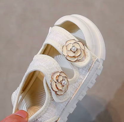 White sandal with floral embellishments held by a hand against a neutral background