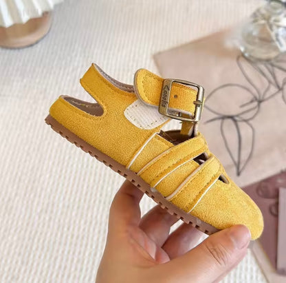 Yellow sandal with a strap held by a hand on a textured surface