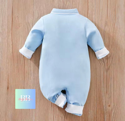 Light blue baby onesie with white cuffs and ankles on a wooden surface, next to a card with 'BB' on it.