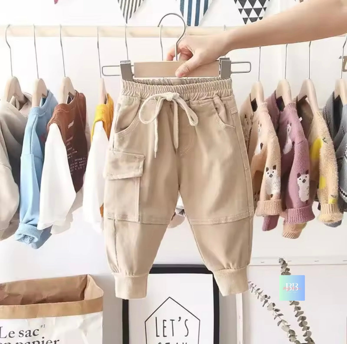 Beige children's pants on a hanger with a background of other children's clothing.