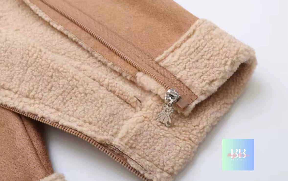 Close-up of a beige fleece jacket with a zipper and a decorative charm on a white background.