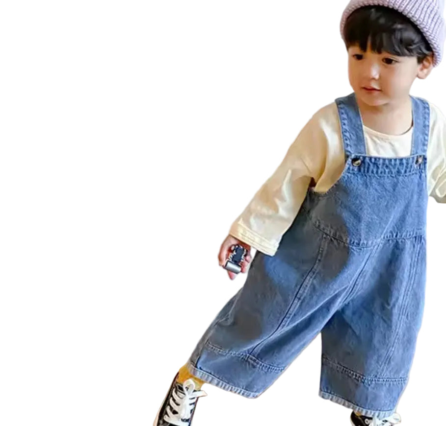 Child wearing a denim overalls and beige jacket indoors on a wooden floor.