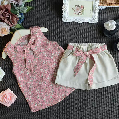 Pink floral top and white shorts with a pink ribbon on a textured surface with flowers and a picture frame.