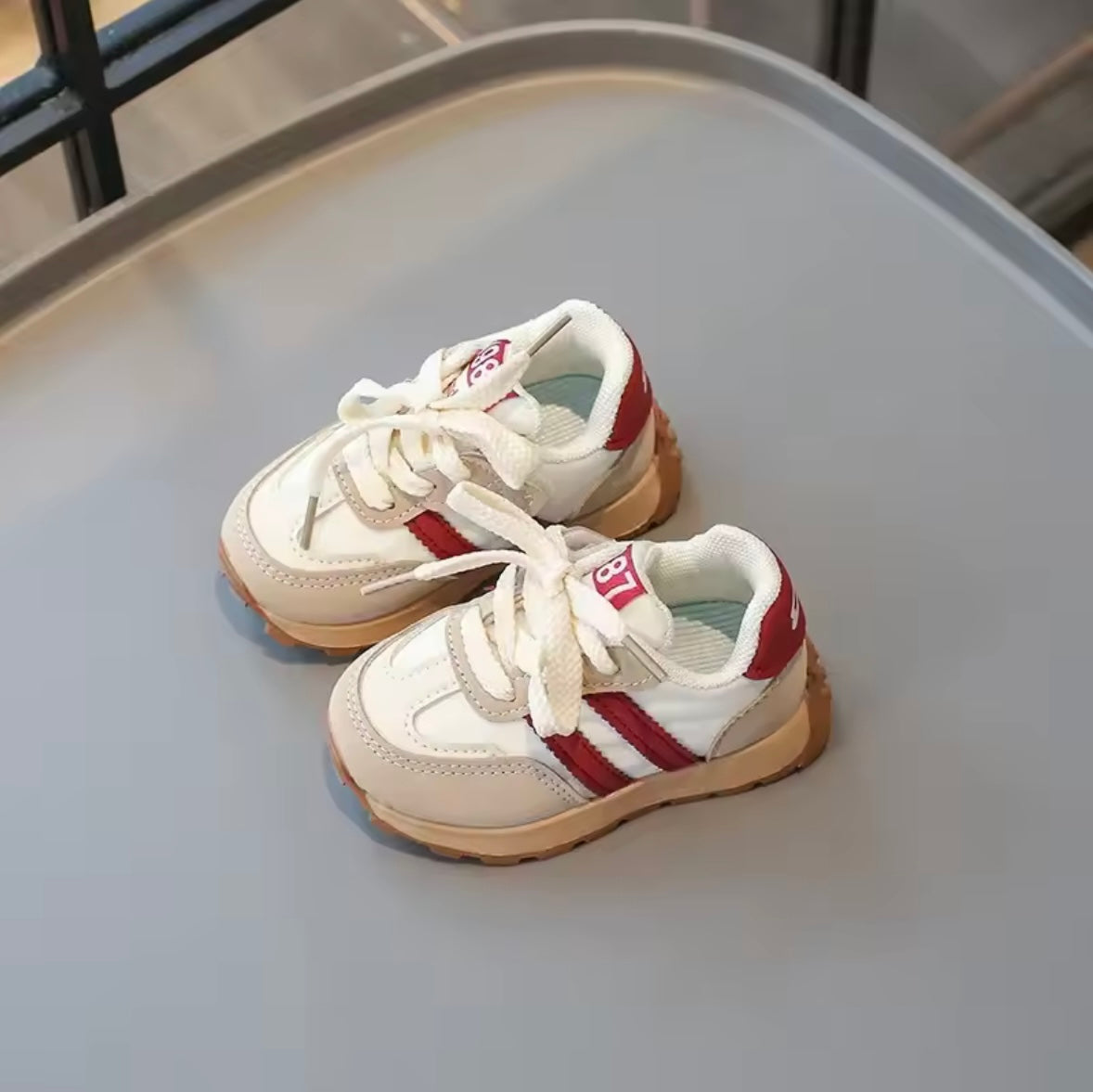 Pair of white sneakers with red stripes on a gray surface
