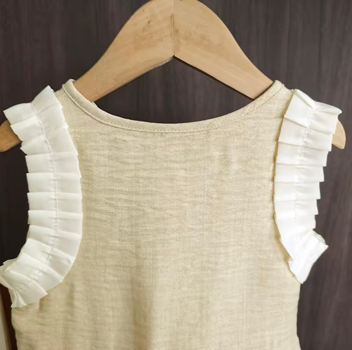 Beige top with white ruffled sleeves on a wooden hanger against a dark background