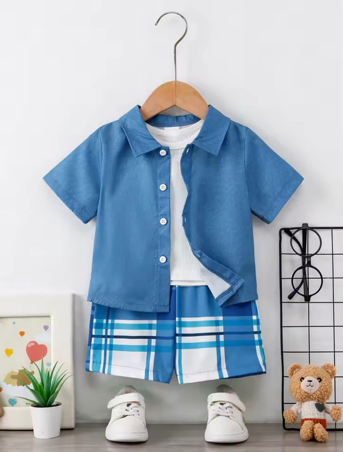 Children's blue shirt and plaid shorts set on a hanger against a white wall.