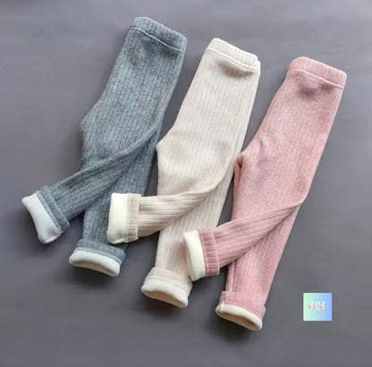 Three pairs of ribbed tights in gray, beige, and pink on a gray background