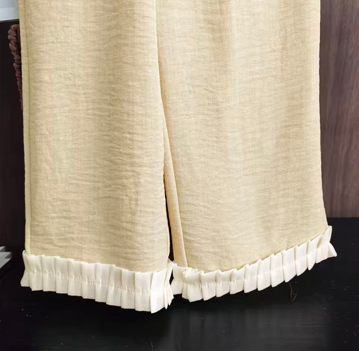 Beige curtain with ruffled hem on a dark background