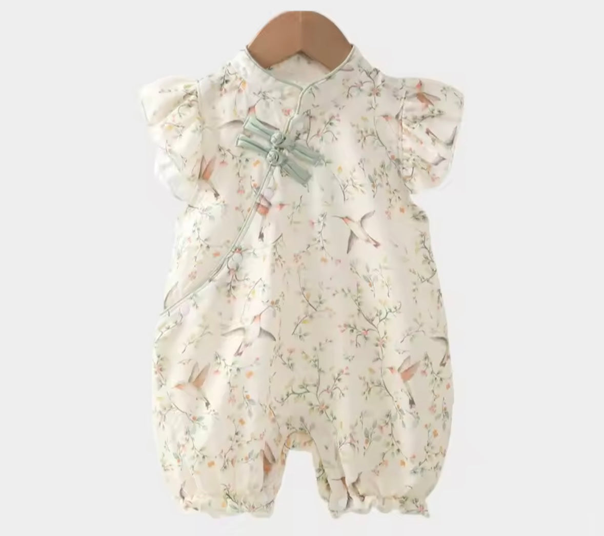 Floral baby romper on a wooden hanger against a white background