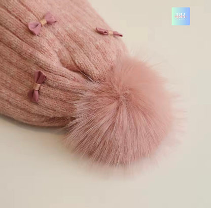 Pink knitted hat with a large fluffy pom-pom on a light background