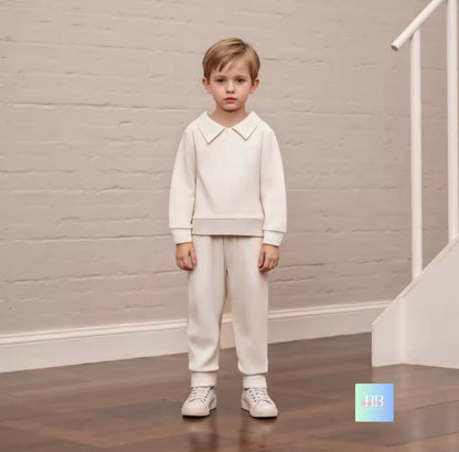 Young boy in a white outfit standing in a room with a neutral background