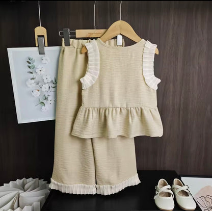Children's beige outfit with ruffled details on a wooden hanger against a dark background.
