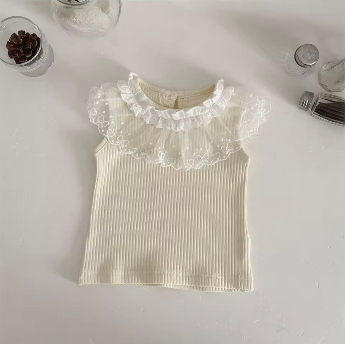 White ribbed tank top with lace collar on a light gray background