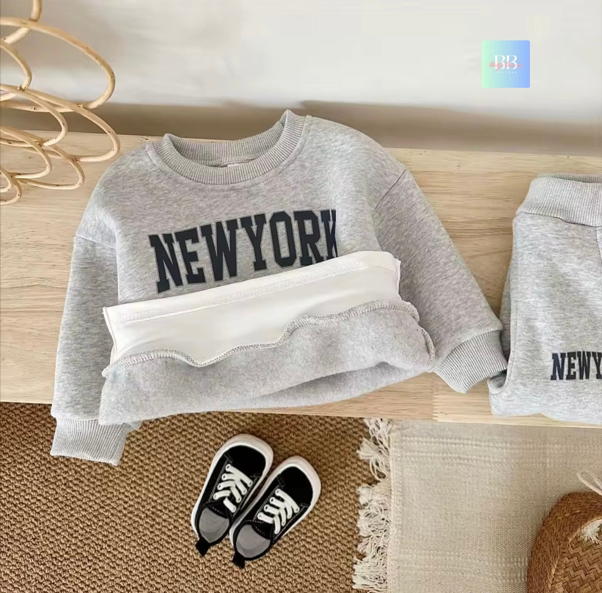 Gray sweatshirt with 'NEW YORK' text on a wooden surface, accompanied by white shorts and black shoes.