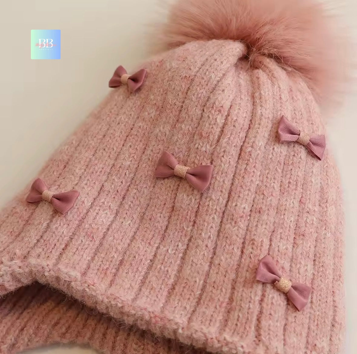 Pink knitted hat with fluffy pom-pom and decorative bows on a light background
