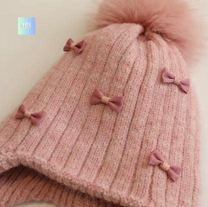 Pink knitted hat with fluffy pom-pom and decorative bows on a light background