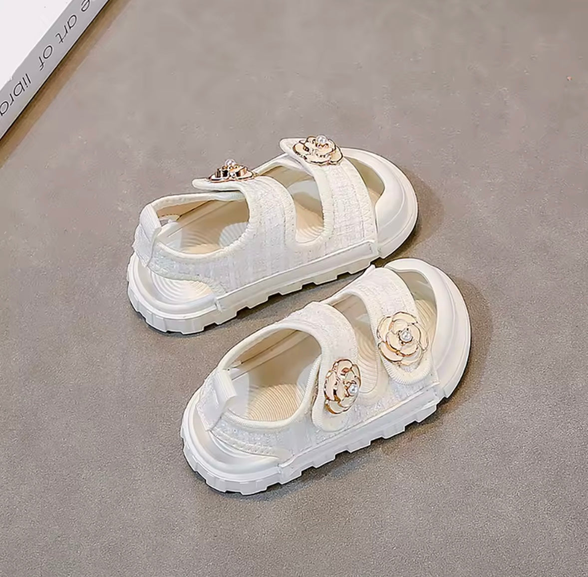 White sandals with floral decorations on a gray surface