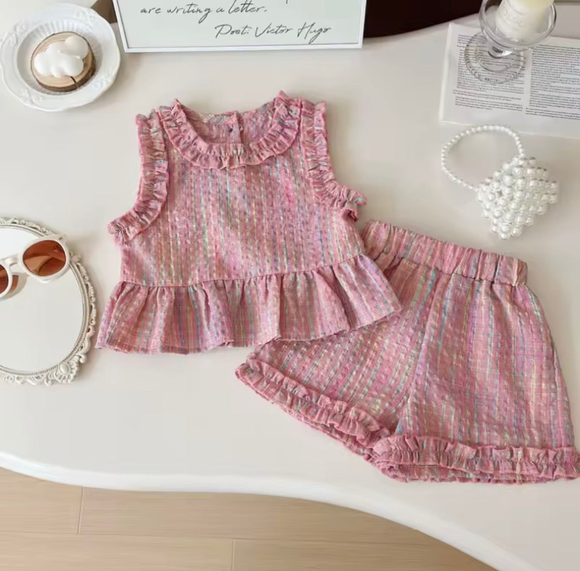 Pink children's outfit with ruffled details on a white surface.