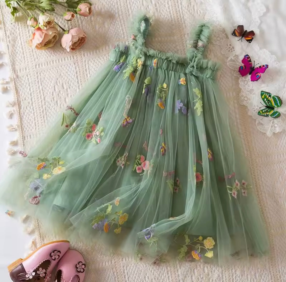 Green embroidered dress on a textured surface with flowers and butterflies.