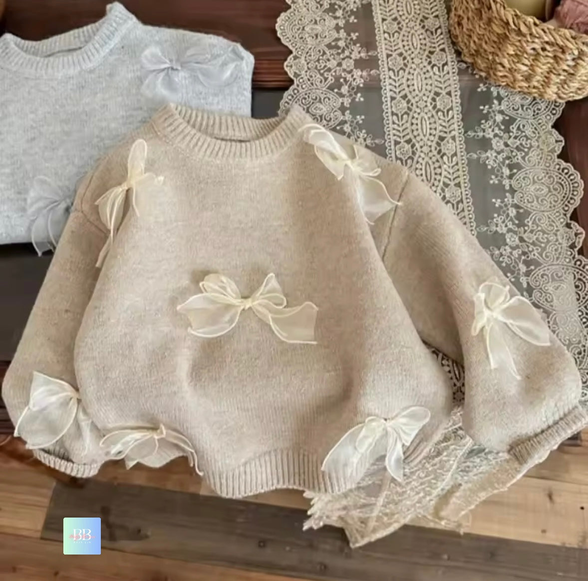 Beige sweater with lace and bow details on a wooden surface