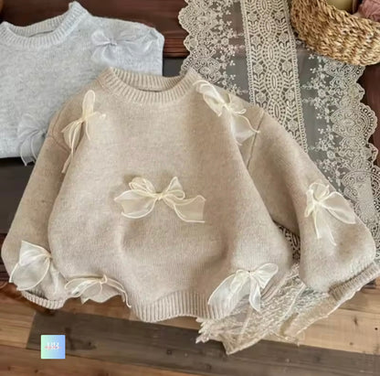 Beige sweater with lace and bow details on a wooden surface