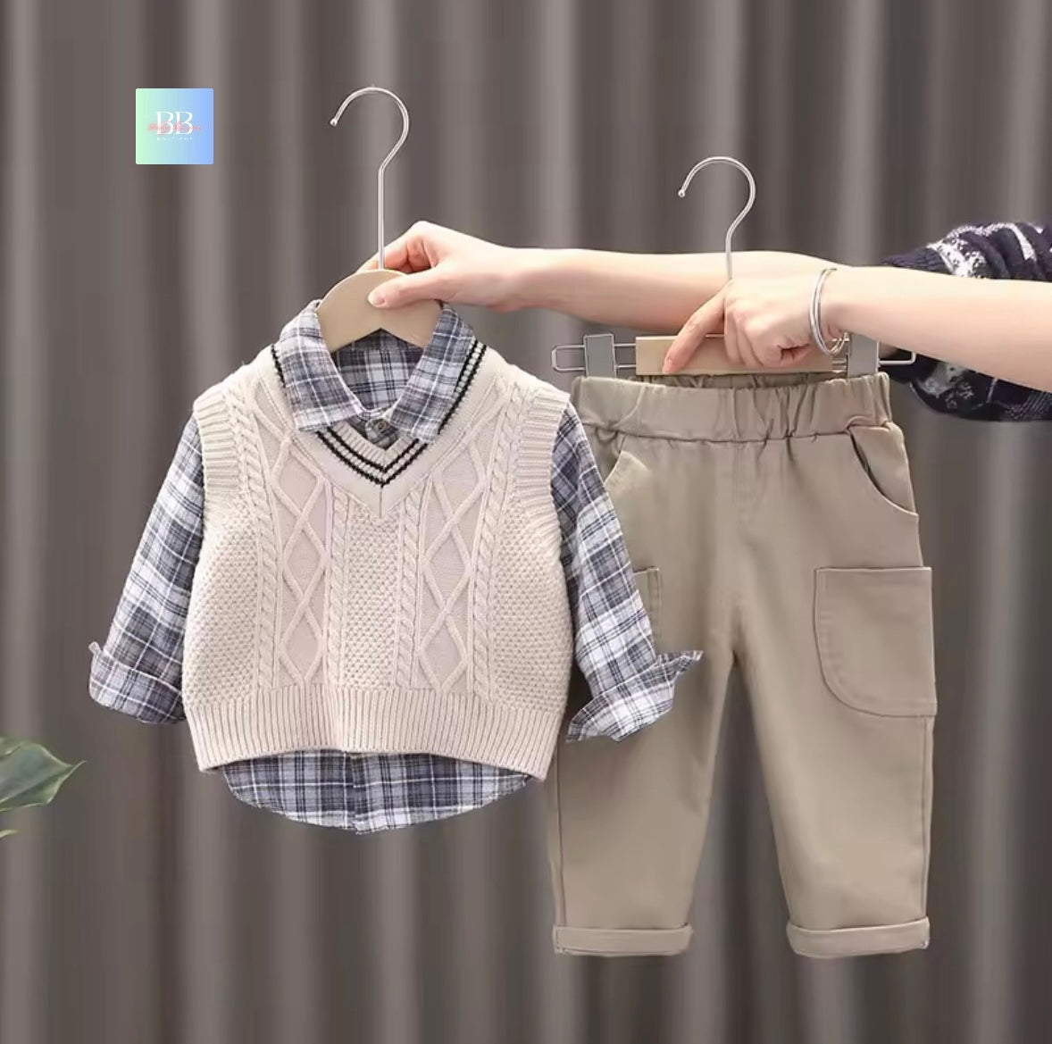 Children's clothing set with vest, shirt, and pants on hangers against a neutral background