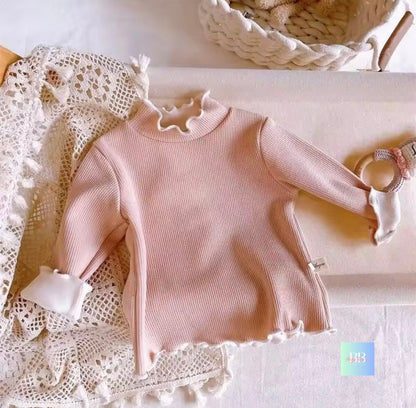 Pink baby sweater with ruffled collar on a lace surface