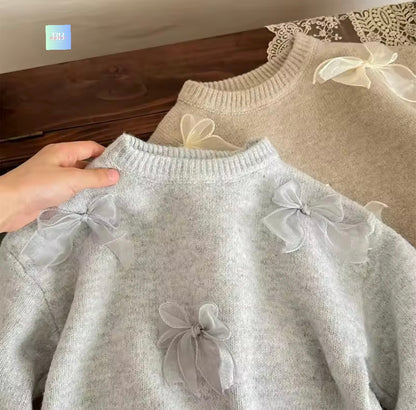 Gray sweater with sheer bow details held by a hand against a wooden surface.