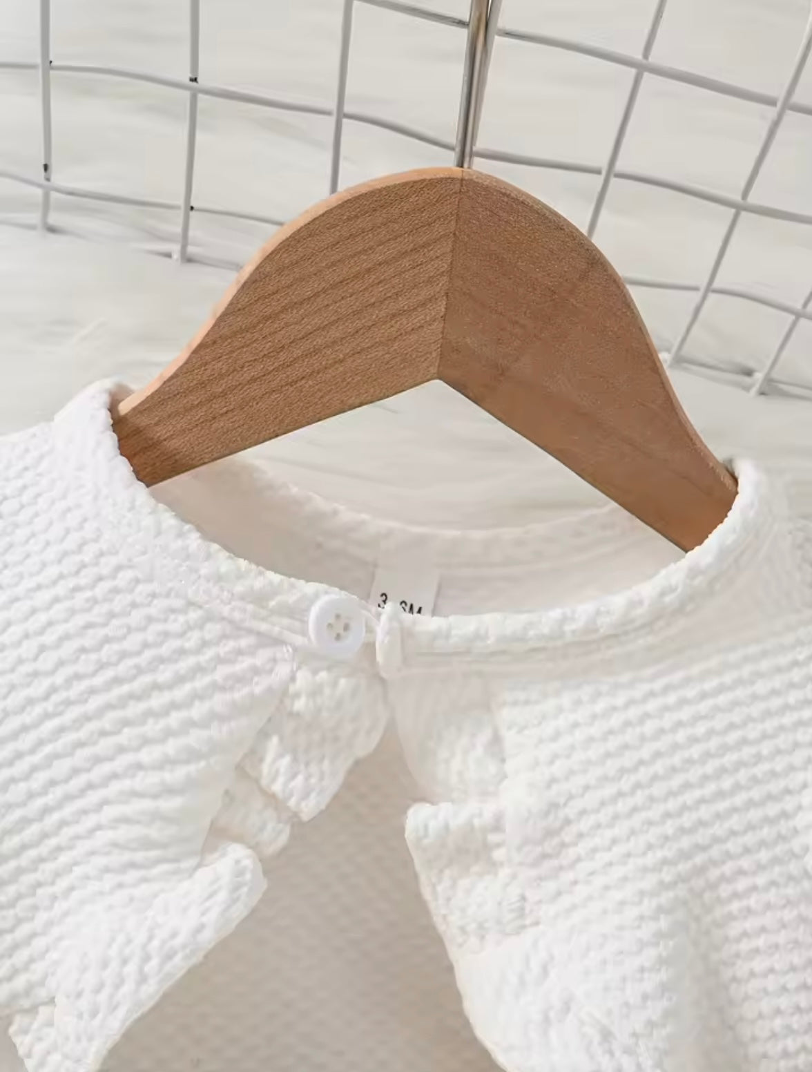 White textured garment on a wooden hanger against a white background