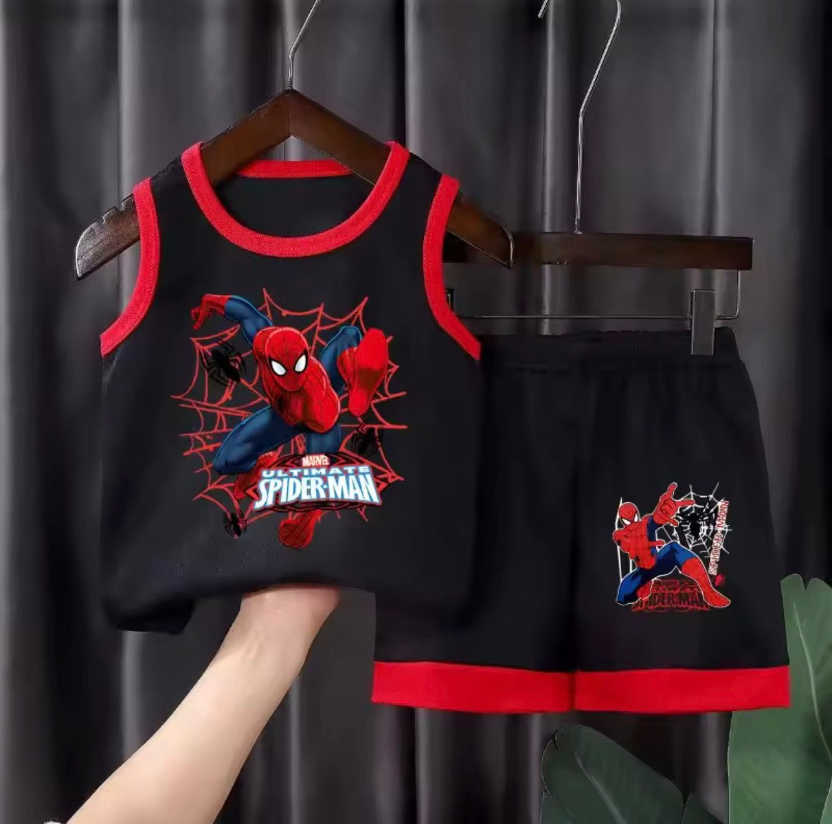 Children's Spider-Man outfit with tank top and shorts on a hanger against a dark curtain background.