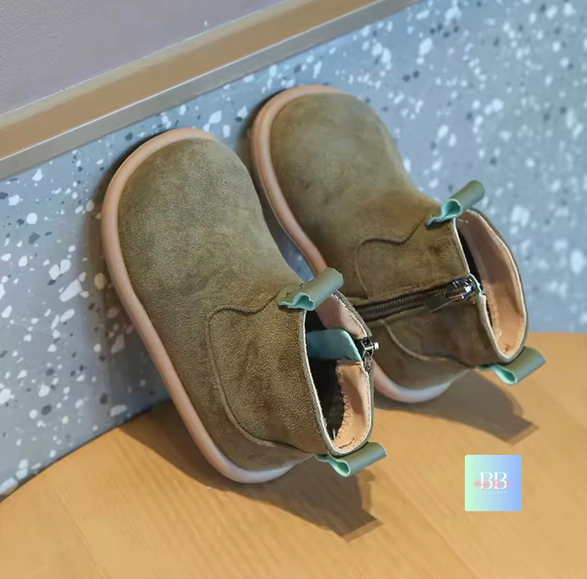 Pair of brown children's boots with green zippers on a wooden surface.