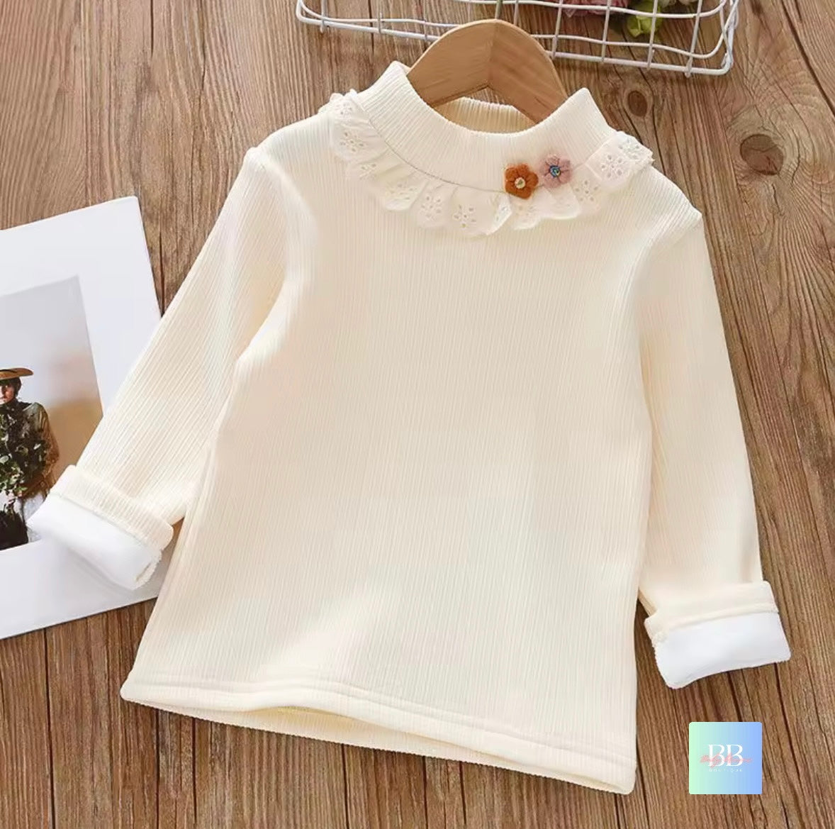 White long-sleeve shirt with lace collar and flower detail on a wooden surface