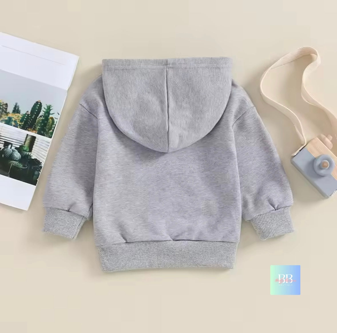 Gray hoodie on a beige surface with a magazine and toy in the background