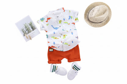 Children's outfit with dinosaur-patterned shirt, orange shorts, white socks, and a hat on a gray background.