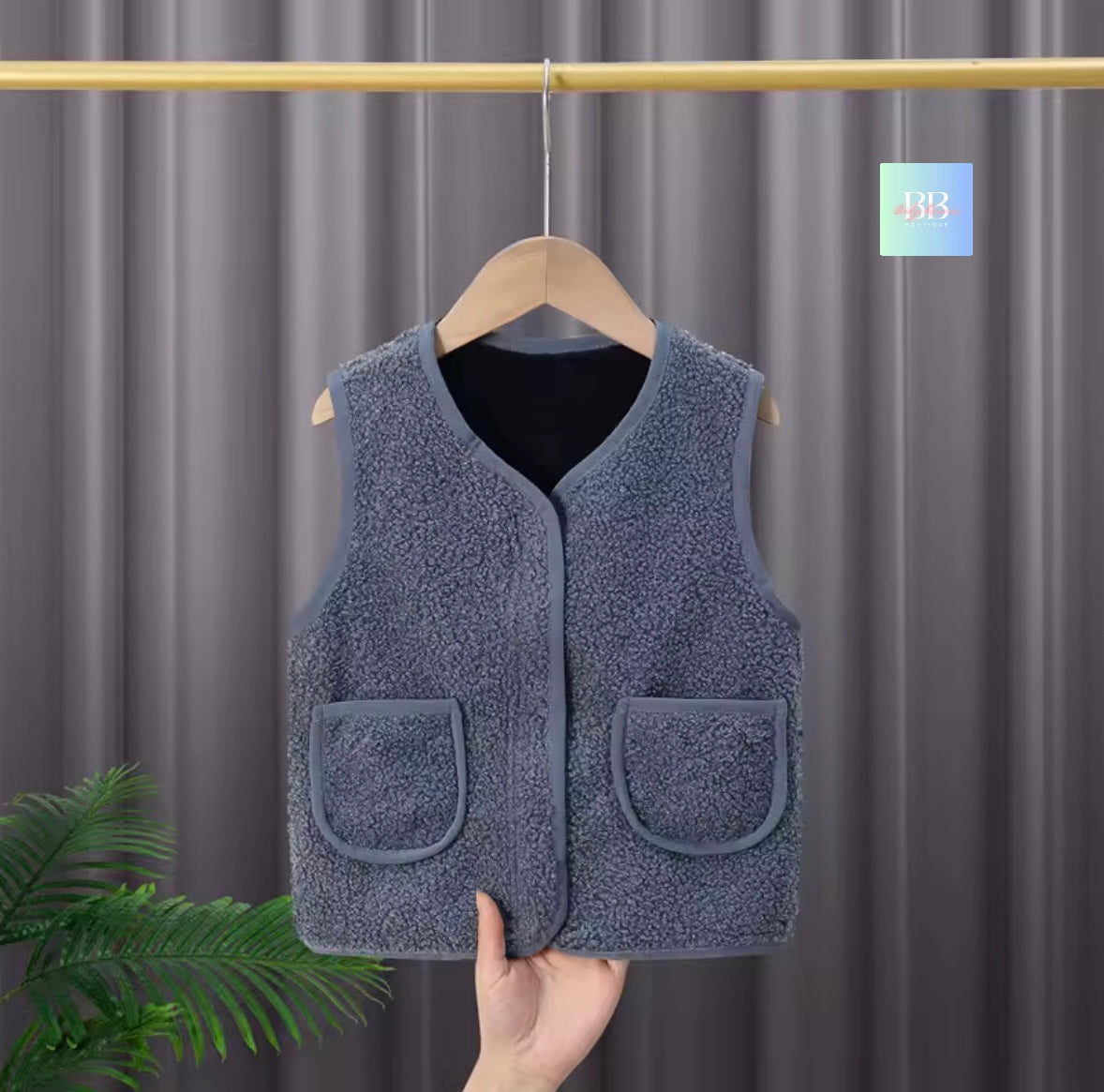 Blue fleece vest on a hanger against a gray curtain background